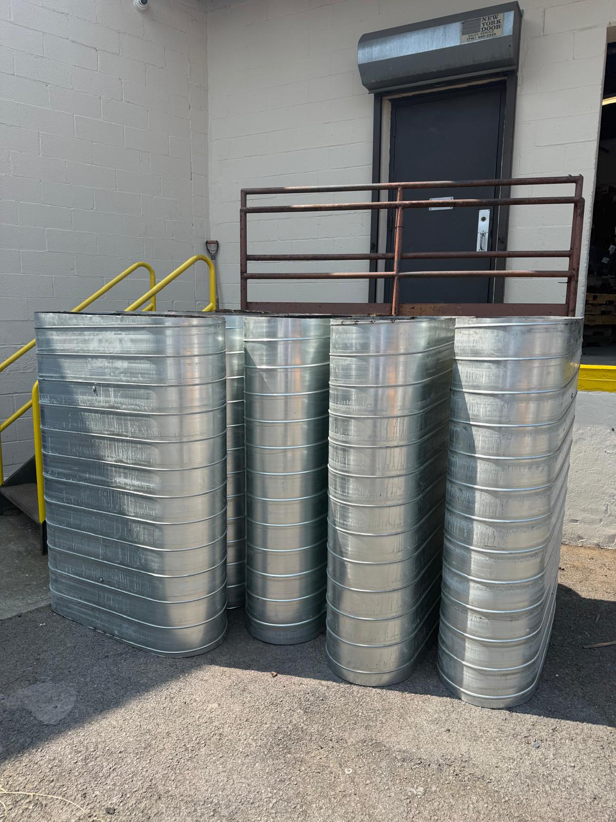 Multiple finished oval duct sections standing outdoors near a loading door