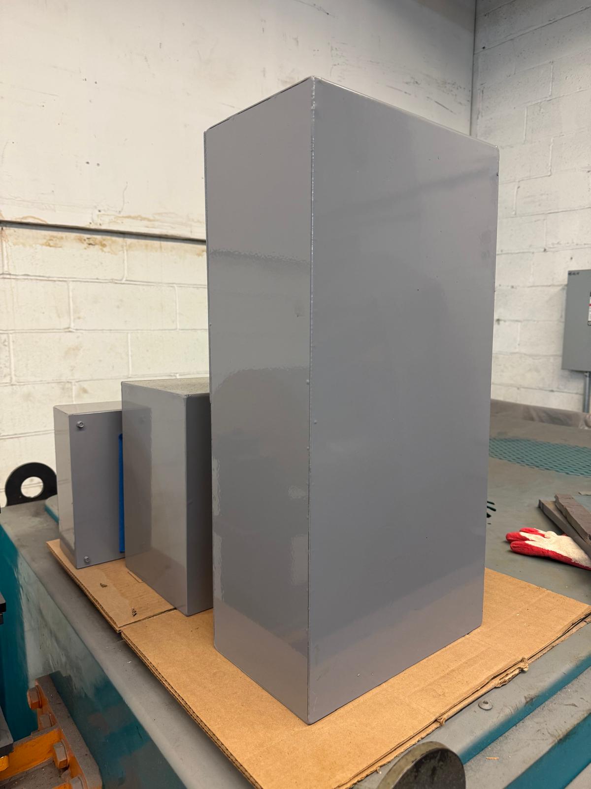 Tall gray metal enclosure beside smaller boxes