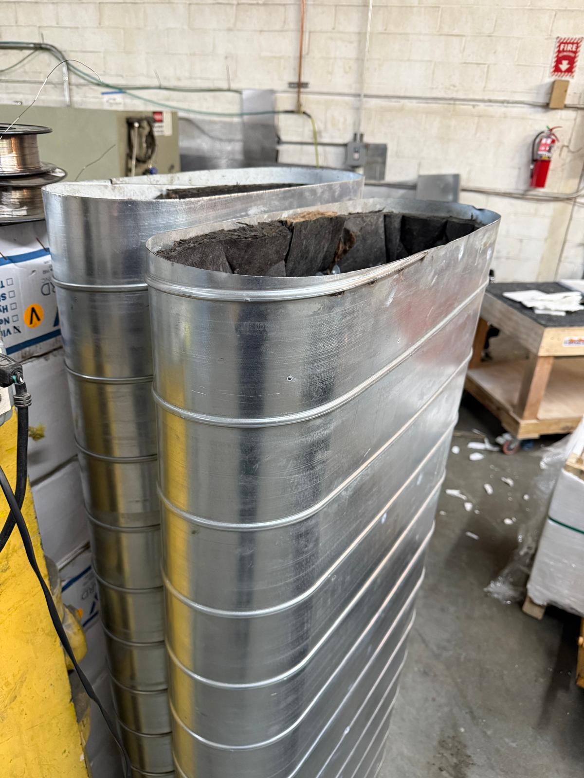 Two tall oval duct sections standing in the fabrication shop